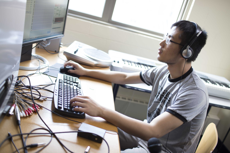 A Case Western Reserve University student seated at a table working on a desktop computer. 